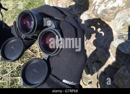 Eine Sonnenfinsternis wird durch ein Fernglas in Lindesfarne gesehen, da eine nahezu totale Sonnenfinsternis heute Millionen begeistern oder enttäuschen wird, je nach Glück und dem unbeständigen britischen Wetter. Stockfoto