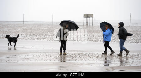 Wanderer kämpfen gegen die Elemente, während Wind und Regen am Karfreitag über den Damm in Lindisfarne, Northumberland, fegen. Stockfoto