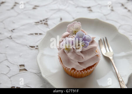 lila Cupcakes mit gezuckerten essbare Blumen auf Vintage Teller Stockfoto