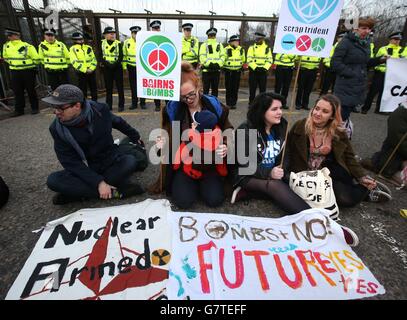 Anti-Trident-Demonstranten sitzen auf der Straße am Eingang des Nordtors am HM Naval Base Clyde, Faslane. Stockfoto