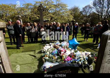Mitglieder der Öffentlichkeit betrachten Blumen und Ehrungen an der Grabseite eines nicht identifizierten Jungen nach einem Trauerdienst auf dem Seafield Cemetery in Edinburgh, fast zwei Jahre nachdem er tot auf einem Pfad gefunden wurde. Stockfoto