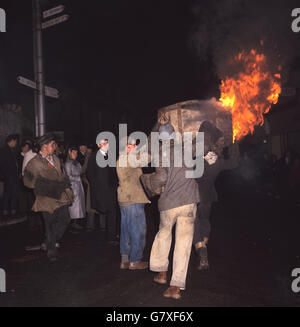 Männer tragen ein brennendes Fass durch die Straßen, während die Menschen darauf blicken. Stockfoto