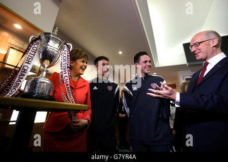 Schottlands erste Ministerin Nicola Sturgeon und der stellvertretende erste Minister John Swinney mit den Heart of Midlothian Football Club-Spielern Angus Beith (zweite links) und Liam Smith (zweite rechts) mit der ersten Division League Championship-Trophäe in Edinburgh nach ihrer ersten großen Wirtschaftsrede seit den Parlamentswahlen. Stockfoto