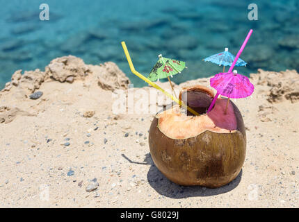 Kokosnuss mit trinken Stroh, Regenschirme und Blumen, auf dem Sand am Meer in Protaras, Zypern-Insel Stockfoto