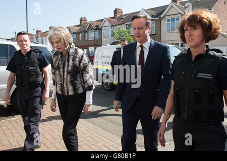 Innenministerin Theresa May (2. Links) und Premierminister David Cameron (2. Rechts) sprechen mit Beamten der Einwanderungsbehörde, nachdem die Beamten Wohnimmobilien auf der Suche nach illegalen Einwanderern in Southall, West London, überfallen hatten. Stockfoto