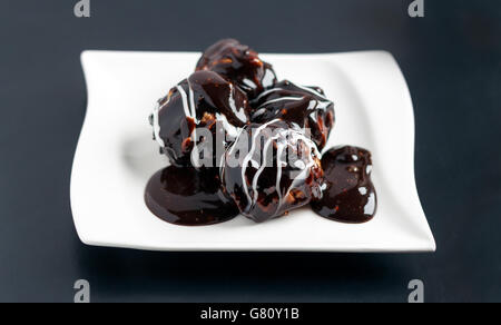 Profiterole Stücke auf einem weißen Teller mit Schokoladencreme und Puderzucker bedeckt Stockfoto