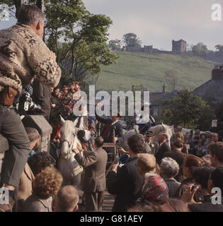 Beim Girlande Day „King“ wird seine Blumengirlande entfernt, während die „Queen“ zuschaut. Die Girlande wird dann auf die Kirchturmspitze gehisst. Peveril Castle ist im Hintergrund. Stockfoto