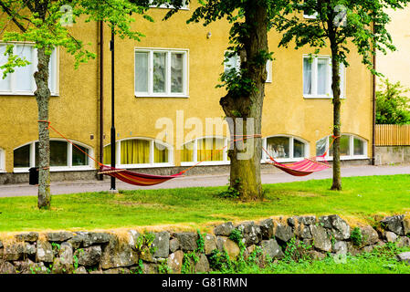 Söderköping, Schweden - 20. Juni 2016: Zwei öffentliche Hängematten zwischen den Bäumen vor einem Mehrfamilienhaus in der Stadt. Stockfoto