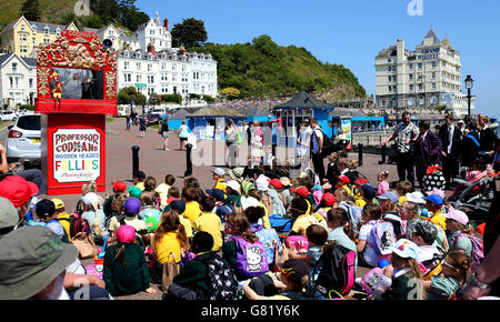 Kinder sehen sich bei warmem Wetter eine Professor Codman's Punch and Judy Show am Ufer von Llandudno in Nordwales an, da am Freitag eine Unwetterwarnung für Gewitter ausgegeben wurde, die der bisher heißeste Tag des Jahres sein könnte. Stockfoto