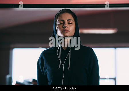 Erschöpfte Frau trägt hooded Hemd stehend mit Augen geschlossen in Turnhalle Stockfoto