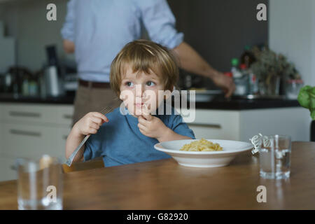Junge essen Nudeln beim Vater arbeitet in der Küche zu Hause Stockfoto