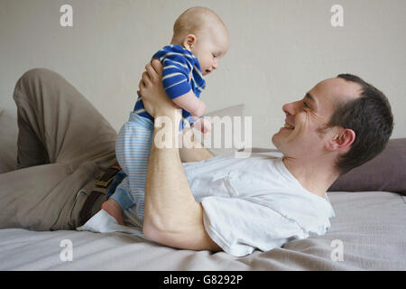 Lächelnden Vater Sohn halten und am Bett zu Hause liegen Stockfoto