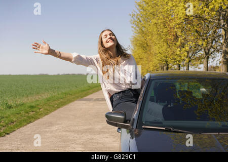 Stets gut gelaunte Frau sitzt am Autofenster am Straßenrand Stockfoto