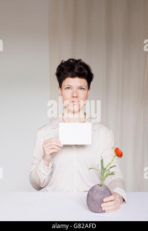 Porträt von Mitte Erwachsene Frau mit leeren Karte und Blumenvase am Tisch Stockfoto