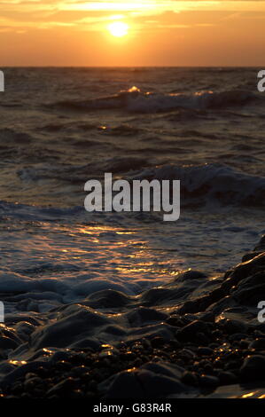 Wellen brechen sich an einem Kieselstrand bei Sonnenaufgang. Dawn unterstreicht die Gischt und Schaum Stockfoto
