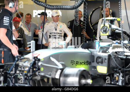 Mercedes-Pilot Nico Rosberg sieht zu, wie Mechaniker in der Teamgarage am Qualifying-Tag für den Grand Prix von Großbritannien 2015 auf dem Silverstone Circuit, Towcester, an seinem Auto arbeiten. Stockfoto
