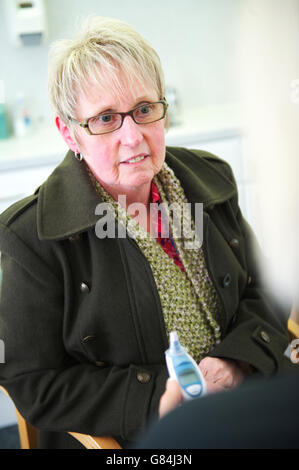 Reife weiße Frau sitzt in ihren Mantel in einem GP Beratungsgespräch mit ihrem Arzt im NHS GP-Gesundheitszentrum Stockfoto