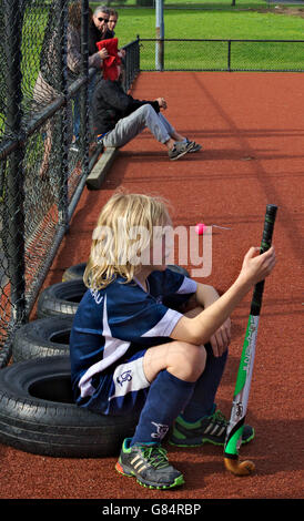 Jungen Hockey-Spieler sitzen auf einem Reifen an der Seitenlinie, starrt auf das Spiel. Stockfoto