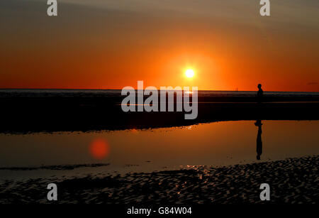 Die Sonne untergeht über einem der Iron Men von Antony Gormley, genannt Another Place, am Crosby Beach, Merseyside, während das warme Wetter in ganz Großbritannien weitergeht. Stockfoto