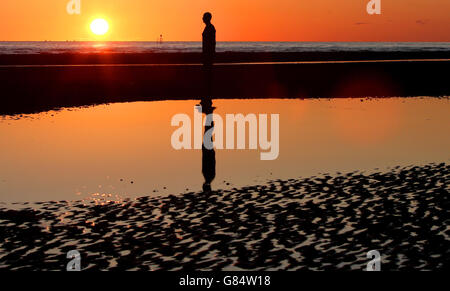 Die Sonne untergeht über einem der Iron Men von Antony Gormley, genannt Another Place, am Crosby Beach, Merseyside, während das warme Wetter in ganz Großbritannien weitergeht. Stockfoto