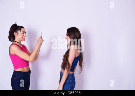 Zwei stilvolle Frauen Spaß mit Handy. Freunde unter Bildern von einander, in städtischen Outfit, isoliert über graue backg Stockfoto