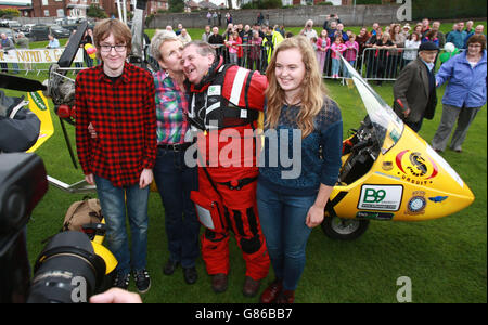 Der nordirische Abenteurer Norman Surplus, der mit dem Gyrocopter einen Rekordflug um die Welt absolviert hat, trifft fünf Jahre nach seinem Start auf dem Cricket-Platz im Bay Park in seiner Heimatstadt Larne ein und wird von seiner Frau Celia, seinem Sohn Felix und seiner Tochter Petra begrüßt. Stockfoto