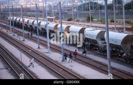 Migranten neben einem Zug, während sie sich auf Schienen in der Nähe des Eurotunnel-Geländes in Coquelles in Calais, Frankreich, zumachen. Stockfoto