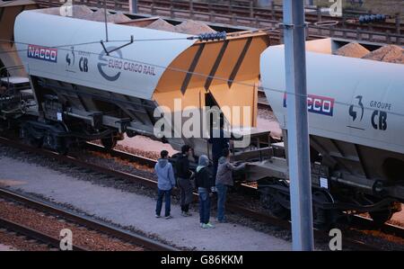 Migranten neben einem Zug, während sie sich auf Schienen in der Nähe des Eurotunnel-Geländes in Coquelles in Calais, Frankreich, zumachen. Stockfoto