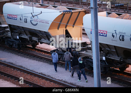 Migranten neben einem Zug, während sie sich auf Schienen in der Nähe des Eurotunnel-Geländes in Coquelles in Calais, Frankreich, zumachen. Stockfoto