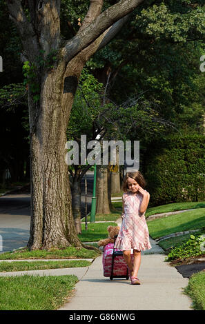 Ein junges Mädchen ziehen einen Koffer auf dem Bürgersteig. Stockfoto