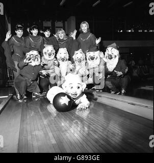 Ken Baker startet als Dopey auf der Bowlingbahn in Wembley, London, in Richtung Pins, wo er in der Eisshow Snow White and the Seven Dwarfs auftritt. Dabei sind seine sechs Gefährten und einige der Showgirls zu sehen. Stockfoto