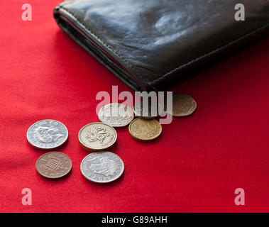 Pfund und Euro-Münzen aus schwarzem Leder Brieftasche verschütten. Roten Hintergrund. Stockfoto