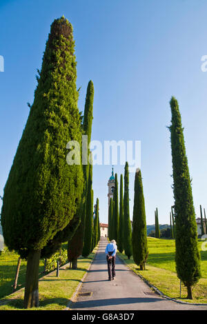 Alte Mann Walkong entlang einer Straße, gesäumt von Zypressen (Cupressus) vor der Kirche von Sant Abbondio in Gentilino Stockfoto