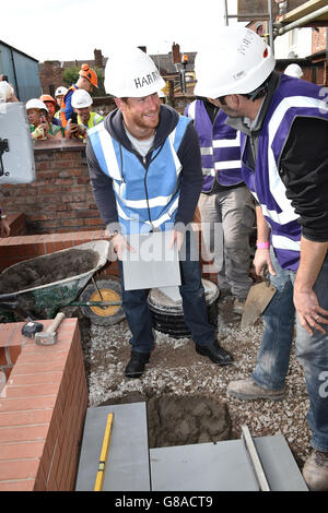 Prinz Harry lächelt, als er sich beim Besuch des DIY SOS-Teams der BBC für das Big Build: Veteran's Special in einer Straße in Manchester auf die Verlegung von Pflasterplatten vorbereitet. Stockfoto