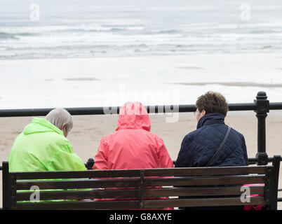 Rückansicht der drei Reife Frauen sitzen auf der Bank mit Blick auf Strand, an einem grauen, kalten Tag in England. UK Stockfoto
