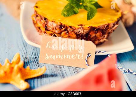 ein braunen Karton Etikett mit Text glückliche Sommer, ein Seestern, einige Scheiben Ananas und ein Stück Wassermelone auf einem blauen rus Stockfoto