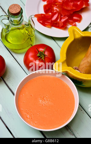 eine Schüssel mit spanischen Gazpacho und einige Zutaten zuzubereiten, wie Tomaten, Knoblauch und Olivenöl, auf einem blauen rustikalen hölzernen ta Stockfoto