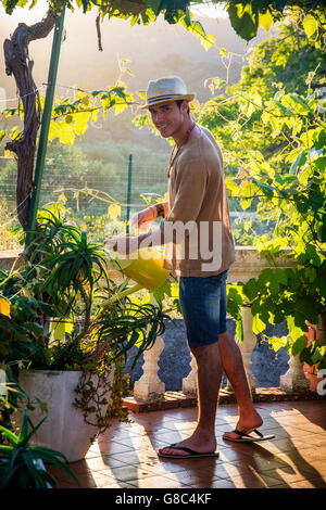 Seitenansicht des stilvollen jungen Mann Bewässerung Pflanzen im Garten in der Sonne Stockfoto