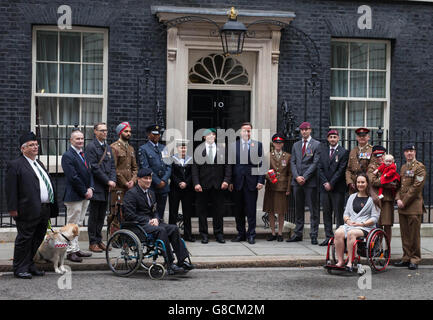 Militärisches Personal, Veteranen und ihre Familien - Alex Noble (Rollstuhl links) und Emma Pack (Rollstuhl rechts) mit (links nach rechts) Alan Hughes, Tom Moreland, Ian Ewers-Larose, Private Harmeet Singh, Flight Sergeant Lenny McKnight, Lois Kelly, Mark Stonelake, Corporal Linda Noble, Lyndon-Walters, Same Taylor im Chat Kapitän Peter Russell, Jodie Older, Sergeant Adam Older mit Baby Isabella Older, bei der ersten Poppy Parade heute - mit dem ersten offiziellen Mohn des diesjährigen Poppy Appeal aus dem Royal British Legion Hauptquartier an Premierminister David Cameron Stockfoto