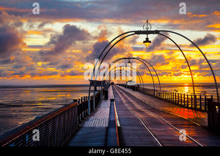 Southport, Merseyside, England.   Großbritannien Wetter. 28. Juni 2016.  Dunkle Gewitterwolken und eine bunte Juni Sonnenuntergang über den viktorianischen Pier-Struktur.  Gerade als die Sonne unterging die Wolken nach starkem Regen nassen Strandsand Rötung und reflektieren die Straßenbahn-Linien schafft eine Illusion einer Resort-Reise in die Unendlichkeit irgendwo heraus über die irische Seeküste entfernt. Bildnachweis: MediaWorldImages/Alamy Live-Nachrichten Stockfoto