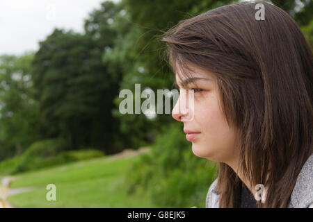 Junge Frau, Erwachsene oder späten Teens, sitzen im Park mit einem feierlichen oder neutralen Ausdruck auf ihrem Gesicht. Stockfoto