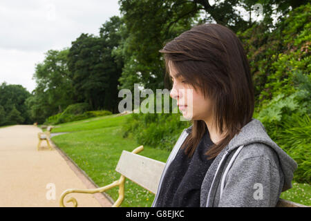 Junge Frau, Erwachsene oder späten Teens, sitzen im Park mit einem feierlichen oder etwas traurigen Ausdruck auf ihrem Gesicht. Stockfoto