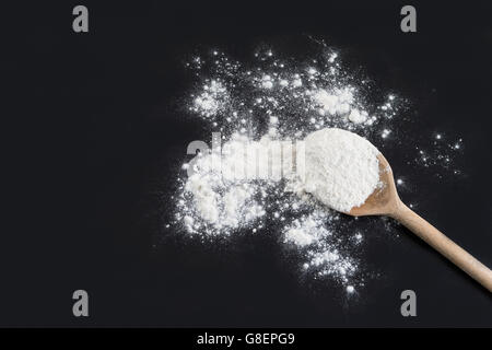 Kochlöffel mit Mehl gegen isoliert auf schwarzem Hintergrund Stockfoto