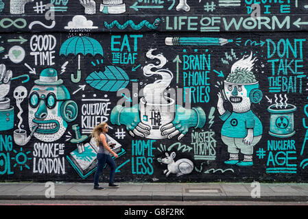Eine junge Frau geht durch ein Stück der Street Art von Italienischen street artist Herr Thoms in Holywell Lane, Shoreditch, East London, UK. Stockfoto