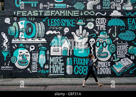 Eine junge Frau geht durch ein Stück der Street Art von Italienischen street artist Herr Thoms in Holywell Lane, Shoreditch, East London, UK. Stockfoto