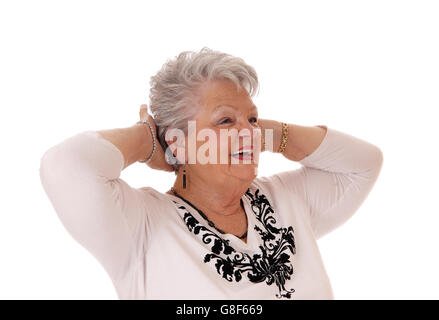 Eine lächelnde glückliche senior Frau in den Siebzigern mit beiden Händen hinter ihrem Kopf stehend für weißen Hintergrund isoliert. Stockfoto