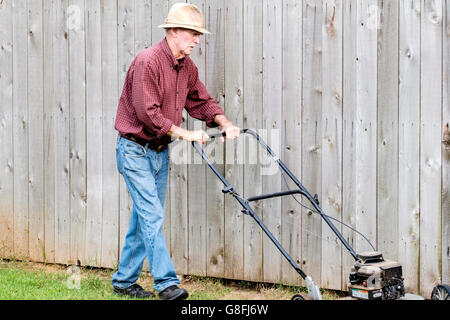 Ein hochrangiger Kaukasier mäandriert im Sommer seinen Rasen mit einem Hut zum Sonnenschutz. USA. Stockfoto