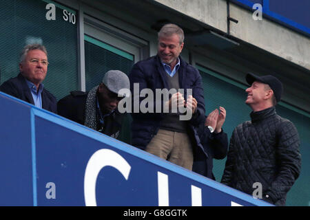 Chelsea-Interimsmanager Guus Hiddink (links) schaut von der Tribüne neben dem ehemaligen Chelsea-Spieler Didier Drogba (Mitte), wie Chelsea-Besitzer Roman Abramovich (rechts) während des Barclays Premier League-Spiels in Stamford Bridge, London, als Chelsea-Score feiert. Stockfoto