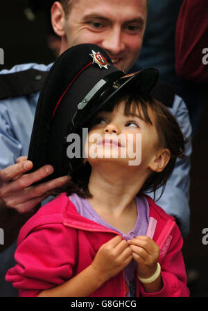 Angelica Niederueyer, 3 Jahre alt, aus New York, zieht den Hut des Feuerwehrkämpfers Paul Austin an, als zwölf Kinder, deren Väter beim Anschlag auf das World Trade Center 9/11 starben, eine Feuerwache in Greenock besuchen. Stockfoto