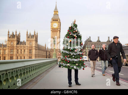 Ein Mann geht über die Westminster Bridge in London, um den Christmas Party Escape Suit zu demonstrieren, ein tragbares Weihnachtsbaum-Kostüm, das den Menschen hilft, diskret langweilige Büropartys zu verlassen - erstellt von LateRooms.com vor morgen, der größten Weihnachtsfeier Nacht. Stockfoto